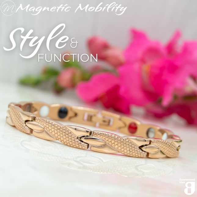 Snapdragon Dawn 4in1 Magnetic Bracelet, rose gold coloured bracelet with snakeskin type designs, designed for pain relief, featuring various therapeutic elements. The bracelet is shown on a reflective surface with a pink flower behind it.