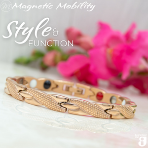 
                  
                    Load image into Gallery viewer, Snapdragon Dawn 4in1 Magnetic Bracelet, rose gold coloured bracelet with snakeskin type designs, designed for pain relief, featuring various therapeutic elements. The bracelet is shown on a reflective surface with a pink flower behind it. 
                  
                